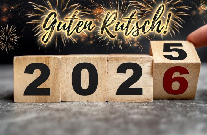 Fotomontage, Neujahrsgruß: Guten Rutsch! in Leuchtschrift zwischen Feuerwerk über Holzwürfeln, die vom Jahr 2025 zu 2026 wechseln
